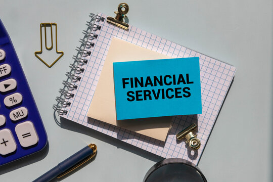 A coloured wooden block with text FINANCIAL SERVICES on it next to white alarm clock.