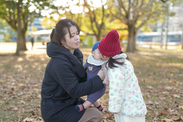 A 3-year-old Japanese girl in a down jacket, a 5-month-old baby and a woman in her 30s kiss while sitting on chairs in a park in Hakata, Fukuoka Prefecture, on a cold winter afternoon.