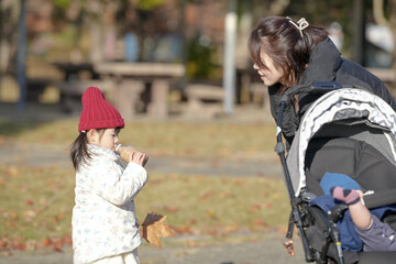 A 3-year-old Japanese girl and a woman in their 30s, wearing down jackets, drink warm milk tea from plastic bottles on a cold winter afternoon in a park in Hakata City, Fukuoka Prefecture.