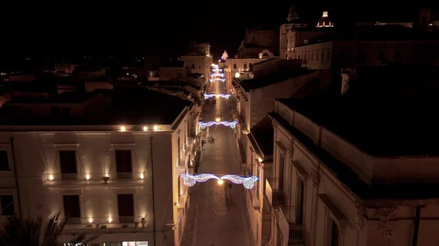 night aerial view of main street of Noto Sicily flying backward over arch