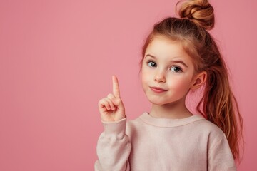 Pretty young girl indicating an empty space with her finger, set against a pink backdrop