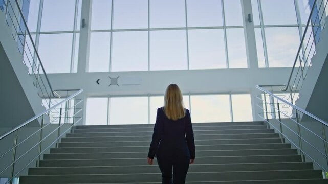 Back view businesswoman walking up stairs inside corporate office. Elegant woman