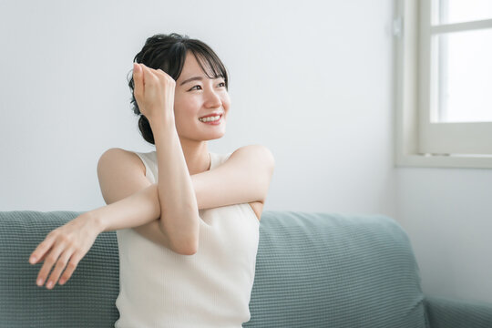 家のソファで軽くストレッチやヨガをする若いアジア人女性（モーニングルーティーン）
