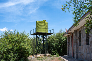 Modern green water raised water tank outside a stone building, in the Maasai Mara National Reserve,...
