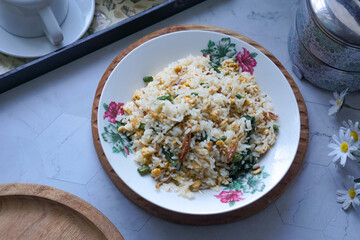 A plate of fried rice garnished with fresh green vegetables and anchovies, served on a floral-patterned plate.  Famously known in Malaysia as Nasi Goreng Kampung.