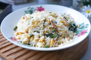 A plate of fried rice garnished with fresh green vegetables and anchovies, served on a floral-patterned plate.  Famously known in Malaysia as Nasi Goreng Kampung.