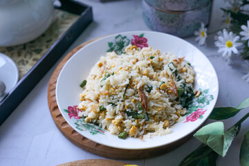 A plate of fried rice garnished with fresh green vegetables and anchovies, served on a floral-patterned plate.  Famously known in Malaysia as Nasi Goreng Kampung.