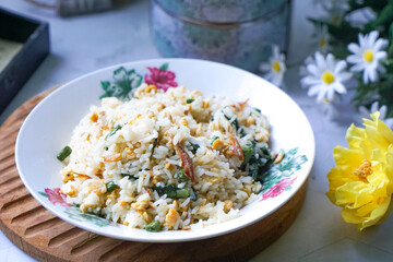 A plate of fried rice garnished with fresh green vegetables and anchovies, served on a floral-patterned plate.  Famously known in Malaysia as Nasi Goreng Kampung.