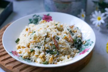 A plate of fried rice garnished with fresh green vegetables and anchovies, served on a floral-patterned plate.  Famously known in Malaysia as Nasi Goreng Kampung.