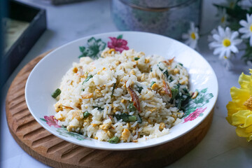 A plate of fried rice garnished with fresh green vegetables and anchovies, served on a floral-patterned plate.  Famously known in Malaysia as Nasi Goreng Kampung.