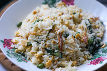A plate of fried rice garnished with fresh green vegetables and anchovies, served on a floral-patterned plate.  Famously known in Malaysia as Nasi Goreng Kampung.