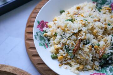 A plate of fried rice garnished with fresh green vegetables and anchovies, served on a floral-patterned plate.  Famously known in Malaysia as Nasi Goreng Kampung.