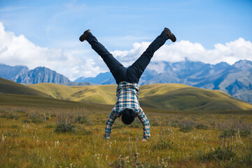 Woman hiker doing a handstand on high altitude mountain top grassland