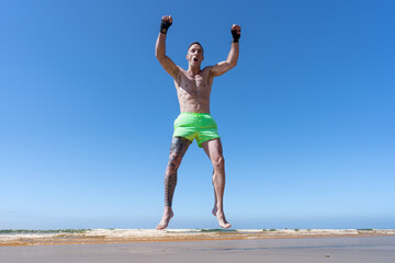 Obraz premium Hombre deportista en kick boxing saltando muy contento con los brazos en alto y los puños cerrados porque ha ganado y es el campeón.