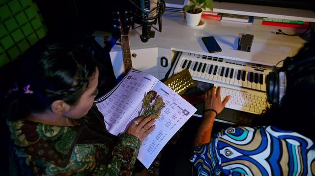 Two artist discuss music sheets front of a computer
