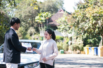 A handsome young Asian Caucasian shop assistant is explaining to a female customer the options for buying a new car and giving a key.