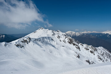 Snow-covered mountain landscape with a blue sky and distant peaks in the background during winter