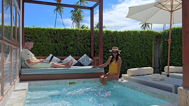 A successful freelancer thrives while working poolside in Thailand, balancing relaxation and productivity in a stunning villa atmosphere. A diverse couple of man and woman at a pool villa,