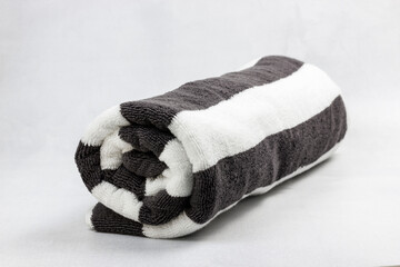 A rolled up black and white striped beach towel isolated on a floor texture background.