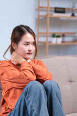 A thoughtful young woman seated on a sofa, resting her head on her hand, appearing deep in...