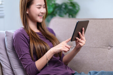 A young woman sitting on a sofa, using a tablet with a smile, enjoying her leisure time at home