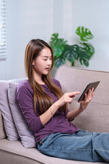 A young woman sitting on a sofa, using a tablet with a smile, enjoying her leisure time at home