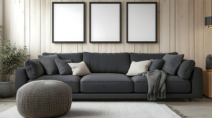 Modern living room interior with dark gray sofa, three empty frames on wooden wall, knitted pouf, and soft rug.