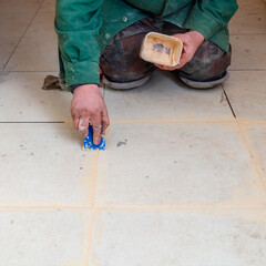 A man is kneeling on the floor and applying a white substance to the tiles