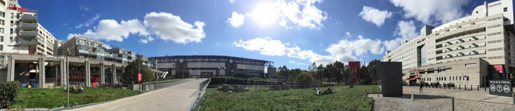 A panoramic view of the Parc des Princes stadium in Paris, home to Paris Saint-Germain Football Club. The stadium is seen from a distance with a walkway and greenery in the foreground.