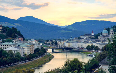 Obraz premium The city of Salzburg with historical buildings bisected by a winding Salzach River and mountain ranges in the background
