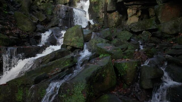 Drone footage of Lumsdale falls streaming on mossy rocks in a steep-sided gorge in Derbyshire, UK