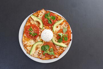 Italian pizza with burrata, tomato and avocado on a black background.