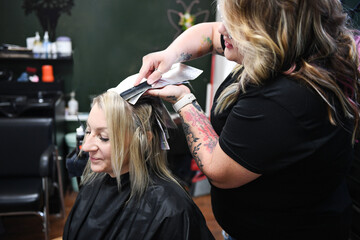 Fototapeta premium Stylist applying foil highlights to client's hair in a salon set