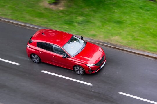 Red Peugeot 308 hatchback car with motion blur effect on wet road