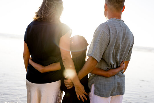 Eight Year Old Girl Embracing Parents on Beach at Sunset in San Diego