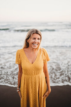 Woman at beach with yellow dress smiling 50 years old