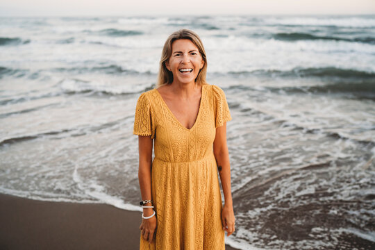 Woman at beach with yellow dress smiling 50 years old