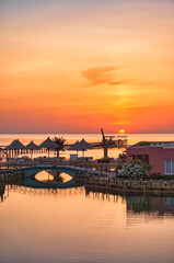 Fototapeta premium Fantastic sunrise in Marsa Alam over the Red Sea. visible palm trees, beach umbrellas, typical hotel buildings. Egypt, Marsa Alam 2024