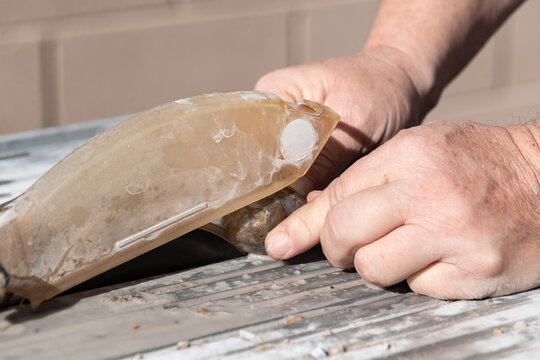 Close up of male man's hands cutting a raw Montana moss agate with a wet rock or tile saw to create slabs for cabbing, lapidary work and jewelry making and geology study