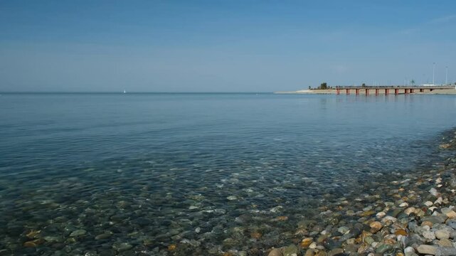 Serene sea view with clear water and pebble shore line near a peaceful pier at midday