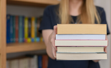 Kobieta stoi w antykwariacie przy polkach z ksiazkami, trzymać w dłoniach stos podręczników 