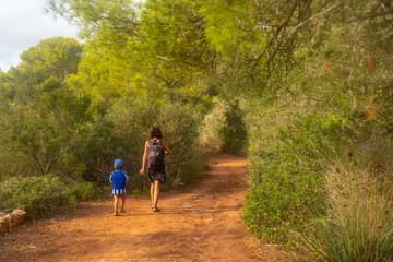 A woman and a child are walking on a dirt path in a forest