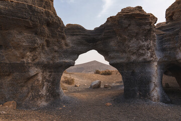 Unique rock formation with a volcanic cone in the background. Lanzarote dramatic landscape.