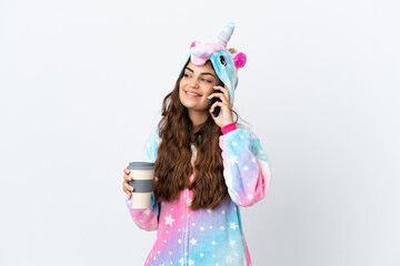 Young caucasian woman wearing a unicorn pajama isolated on white background holding coffee to take away and a mobile