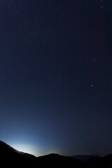 A winter night sky full of twinkling stars spread out over the ridge. Pleiades Cluster and Jupiter
