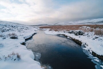 A tranquil river flows gently in a snowy landscape, with fields of dried grass and rolling hills covered in a white blanket. The sky features soft clouds, adding to the serene atmosphere.