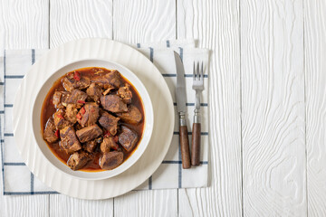 beef stew in a white bowl on rustic wooden table