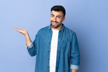 Caucasian man over isolated blue background holding copyspace imaginary on the palm to insert an ad