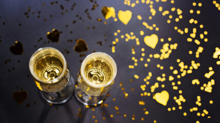 Two glasses of champagne and golden confetti on black background. Celebration, festive, party time concept. Christmas, New year's eve, Valentines day. Above view