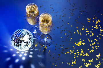 Two glasses of champagne, disco ball and golden confetti on dark blue background. Celebration, festive, party time concept. Christmas, New year's eve, Carnival, masquerade.